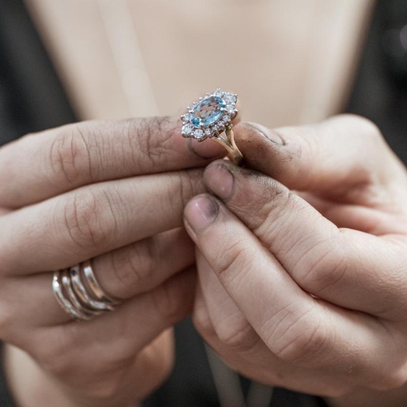 Custom aquamarine engagement ring with diamond halo in jeweller's hands